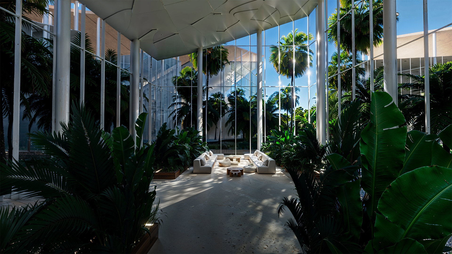 Espace lounge intérieur lumineux au cœur de la COP16, avec canapés blancs, végétation tropicale et grandes baies vitrées ouvertes sur des palmiers