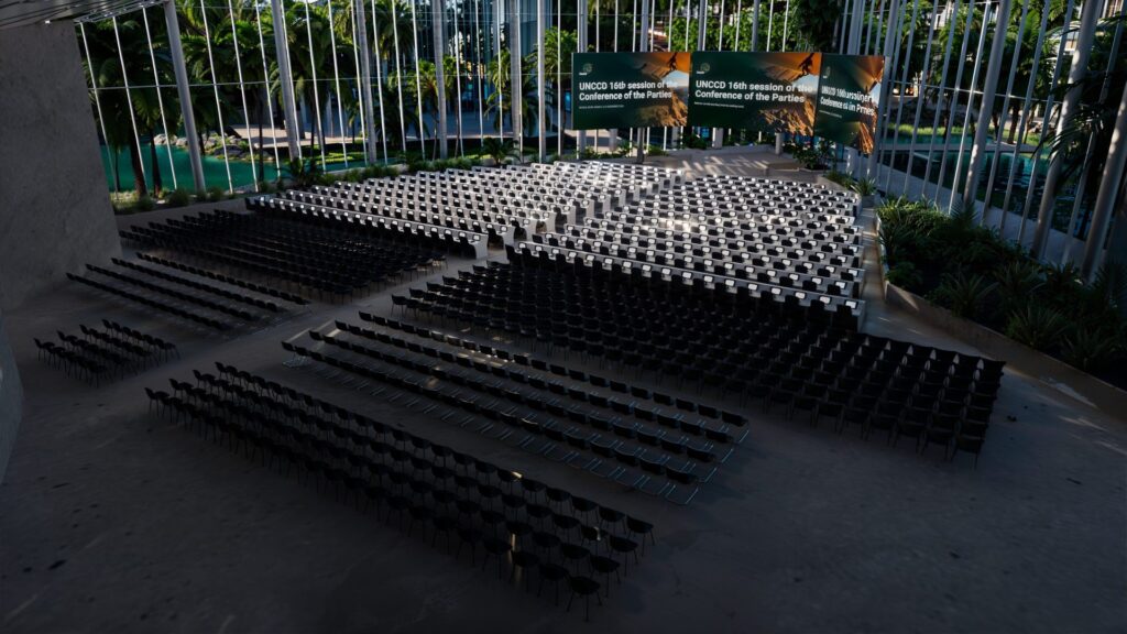 Vue panoramique d'un amphithéâtre moderne prêt à accueillir la 16e session de la COP sur la désertification, avec rangées de sièges alignées et écrans LED en fond.
