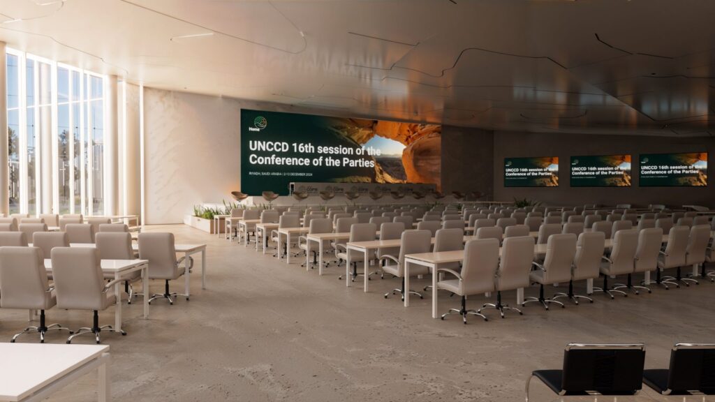 Salle de conférence intérieure pour la COP16 avec mobilier haut de gamme, éclairage naturel et écrans affichant la session des Nations Unies sur la désertification