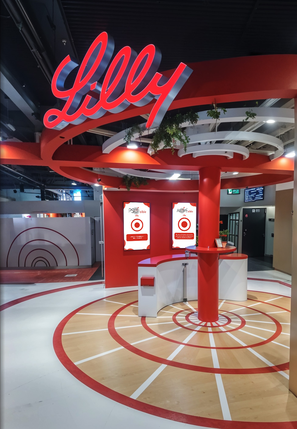 Vue d’ensemble du stand Lilly conçu pour le congrès du SFD 2024 au Palais des Congrès de Paris. L’installation circulaire, visuellement marquante, combine un plafond suspendu à géométrie radiale, un branding immersif en 3D et un espace central dédié à l’interaction. L’architecture scénographique, signée Face X, intègre des éléments ludiques et symboliques (comme la cible au sol) pour orienter naturellement le visiteur vers le dispositif de jeu.